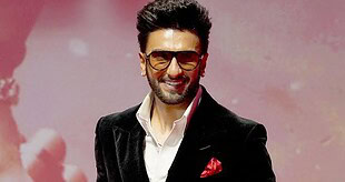 Man wearing sunglasses, black blazer, and white shirt smiling at event.