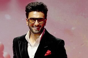 Man wearing sunglasses, black blazer, and white shirt smiling at event.
